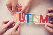 The word autism written on a piece of paper being held by several different hands
