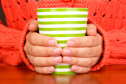 Close up of hands hugging a warm drink in a stripey mug. The person is wearing an orange jumper.