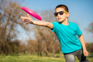 young boy with sunglasses on throwing a pink frisbee in a park