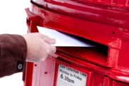 Hand posting a letter into a red postbox