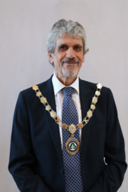 older gentleman with grey hair and beard wearing suit and ceremonial chains