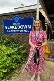 Lady stood in front of school sign holding litter picking equipment