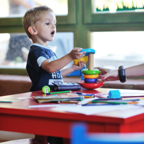 A young boy plays with a stacking toy in a classroom