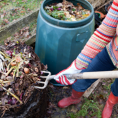 Someone in a striped jumper uses a garden fork to put garden waste into a compost bin