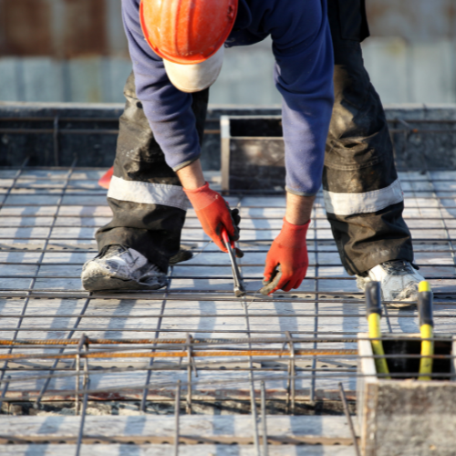 A man wearing a hard hat works on some metal and concrete on a construction site