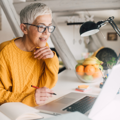 A grey haired woman sits looking at her laptop