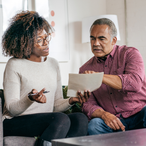 Two adults sit on a sofa and look at a document together