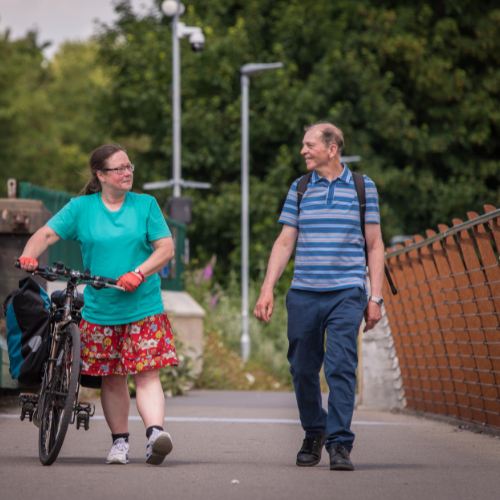 A woman pushing a bike walks alongside a man as they cross a bridge