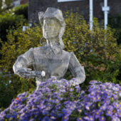 One of the ghost sculptures made of metallic wires against a backdrop of flowers in a garden