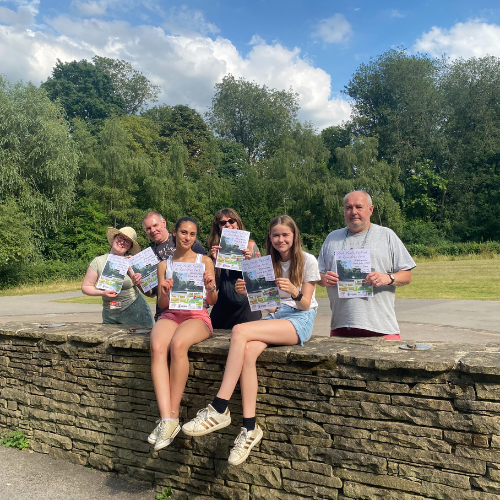 Group of people sat on a wall holding posters advertising the York Youth Festival