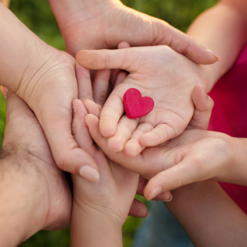 Hands of adults and children reaching out to hold a heart shape.