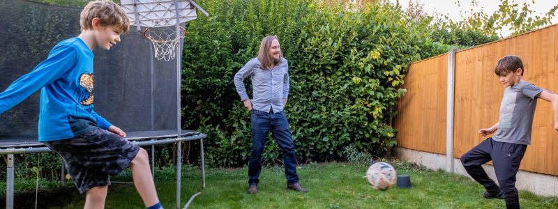 Two boys and a man play football in a back garden