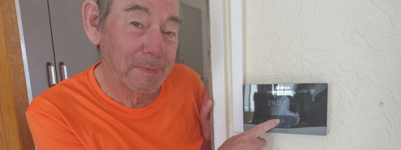 A smiling man points at a thermostat