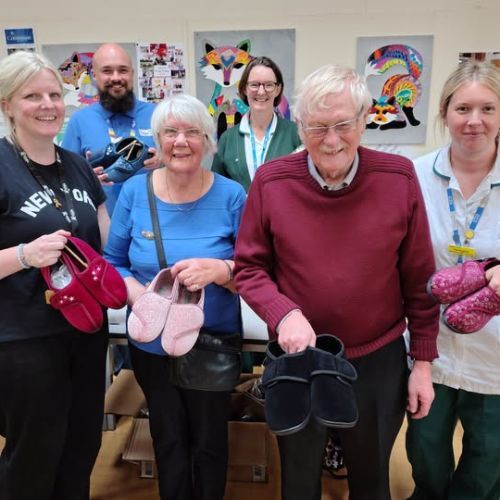 A group of smiling people each holding a pair of slippers
