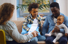 Social worker consulting smiling young single father with kids at home.