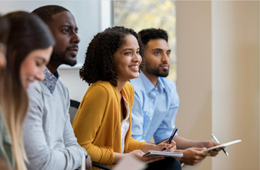 Four professionals sitting in a row, taking notes while listening to a presentation. 