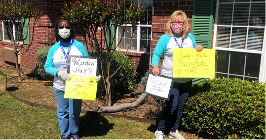 Two women wearing face masks holding signs outside a building