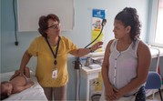 A medical professional tells a woman about Zika while examining her infant child.