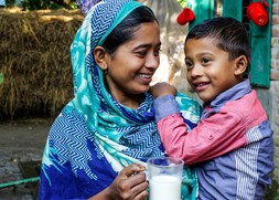 Mother and child smile while holding a glass of milk in Bangladesh.