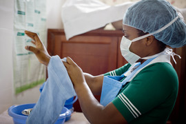 Health worker in Ghana washes hands while wearing a face mask.