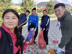 Five high school youth smile for a selfie. Wearing plastic gloves, they hold red trash bags to collect trash in their rural town. 
