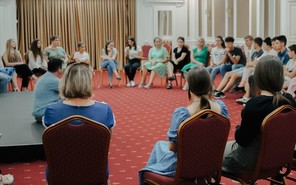 A large group of volunteer training participants sit on chairs in a semi-circle to discuss.
