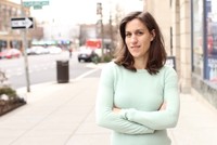 A woman stands on a city sidewalk with her arms crossed.