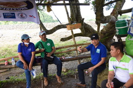 Partners and project participants of GROW CO-OP sit on benches under a tree outside a farm.