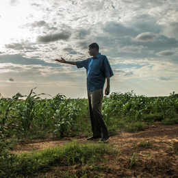A man in profile stands in a field, one arm outstretched.