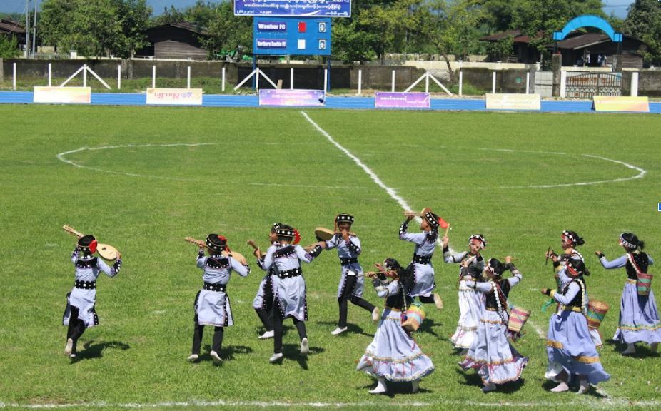 Burmese cultural group perform a dance on a green field