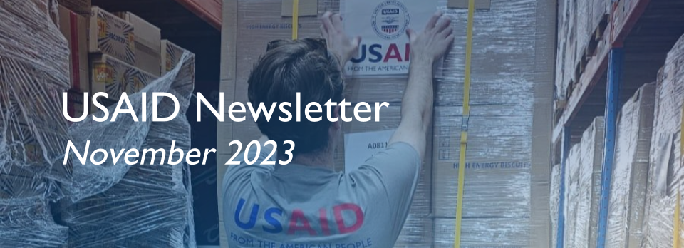 A person in a USAID shirt places a USAID logo label on boxes of aid. 