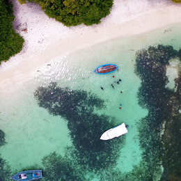 Aerial shot of ocean scene in the Maldives. Three boats float in the water as people swim.