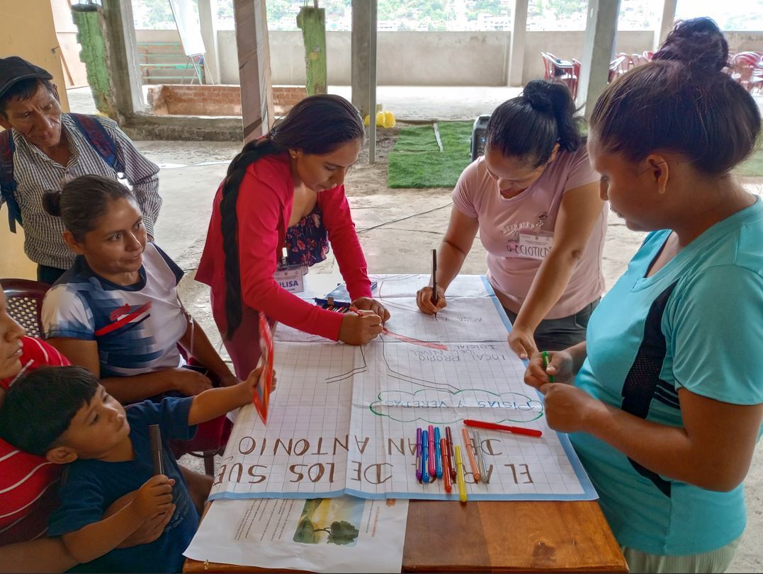 Six people from the Ayna community huddle around a poster writing with markers to map out their vision.