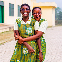 Two students dressed in matching green dresses smile and pose together in an embrace.