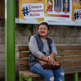 A woman sits on a brown bench below awareness posters