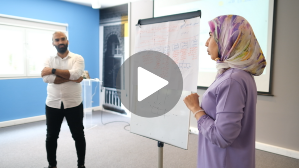 A woman and man from Morocco stand near a flip chart presenting to a room