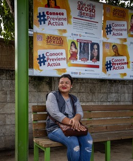 Activist  sits in front of a bus station plastered with signs 