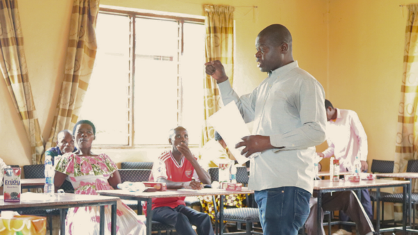 Pamodzi Blantyre District Coordinator stands talking to individuals seated at tables as he guides a scorecard session.