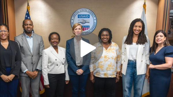 FSN Localization Fellows pose with Samantha Power and Paloma Adams-Allen in front of flags and the USAID seal.