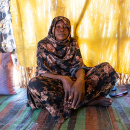 A Sudanese woman sits cross-legged on a floor. 