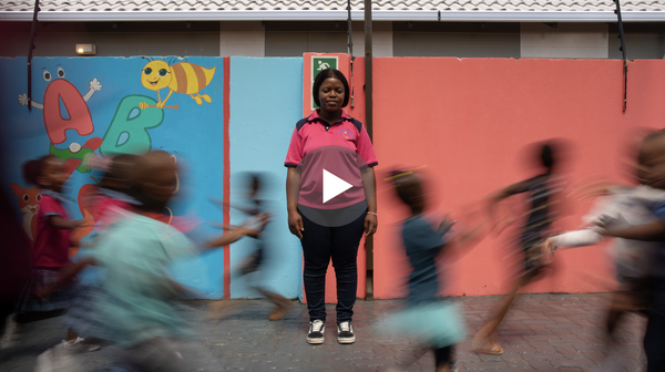 A woman in a pink shirt stands as children run around her