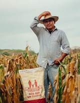 A farmer standing in his field with a bag of Fortaleza F3 biofortified seed.