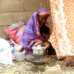 A woman in a purple garment sits on the ground peeling a potato.