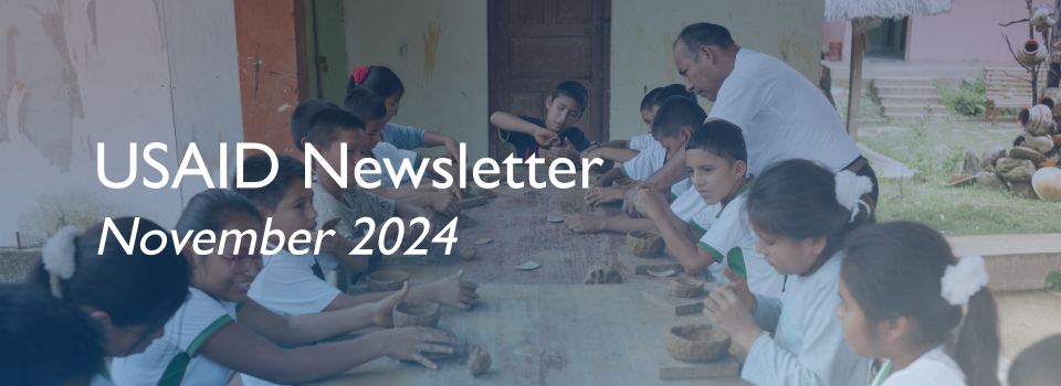 Children in white shirts sit at a table, sculpting pottery with clay. 