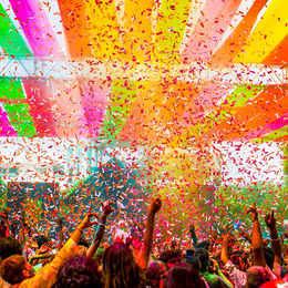 A crowd of people standing under colorful banners and falling confetti