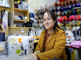 woman seamstress sitting in her sewing workshop surrounded by threads and a sewing machine