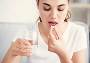 Woman taking pill and holding glass of water.