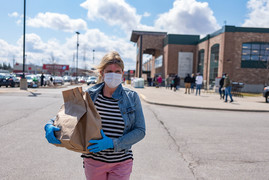 A woman wearing a face mask as protection against COVID-19 walks back to her car with a bag of groceries.