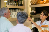 A worker at the bakery counter of a restaurant packs up baked goods for an older couple.