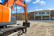 A bright orange construction excavator in the recently graded parking lot of a new high school.